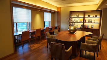 A conference room with a round table, chairs, a bookshelf, and a window with blinds.