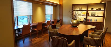 A conference room with a round table, chairs, a bookshelf, and a window with blinds.