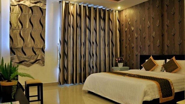 A modern bedroom with a large bed, a nightstand, a potted plant, and a decorative wall panel. - Manh Cuong Hotel (Da Nang)