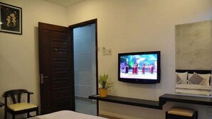 A hotel room with a bed, a television mounted on the wall, a desk with a chair, and a door. - Manh Cuong Hotel (Da Nang)