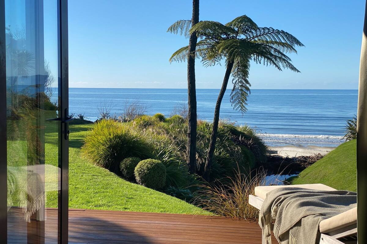 A room with a view of the ocean, a wooden deck, and a bed with a blanket.