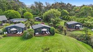 A cluster of modern houses with outdoor seating areas, surrounded by lush greenery and trees. - Adrift In Golden Bay (Parapara)