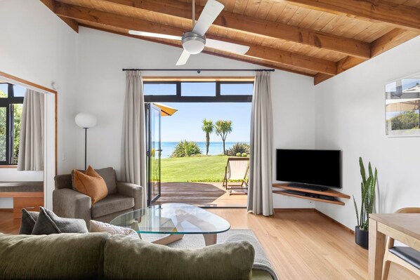 A modern living room with a glass coffee table, a sofa, a television, and a view of the ocean. - Adrift In Golden Bay (Parapara)