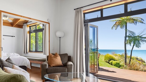 A modern living room with a glass table, a sofa, and a view of the ocean. - Adrift In Golden Bay (Parapara)
