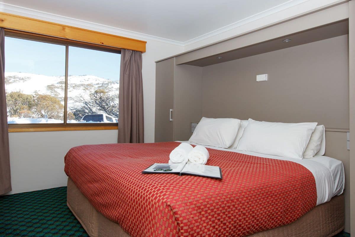 Een hotelkamer met een groot bed, een raam met gordijnen en uitzicht op besneeuwde bergen.