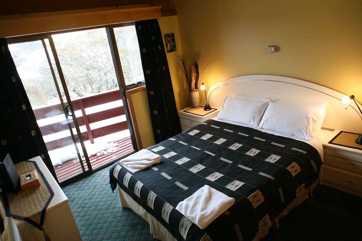 Een hotelkamer met een bed, nachtkastje, lamp, raam met gordijnen en uitzicht op de omgeving.