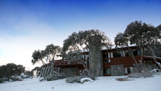 A modern building with a stone facade and wooden beams, surrounded by snow-covered trees.