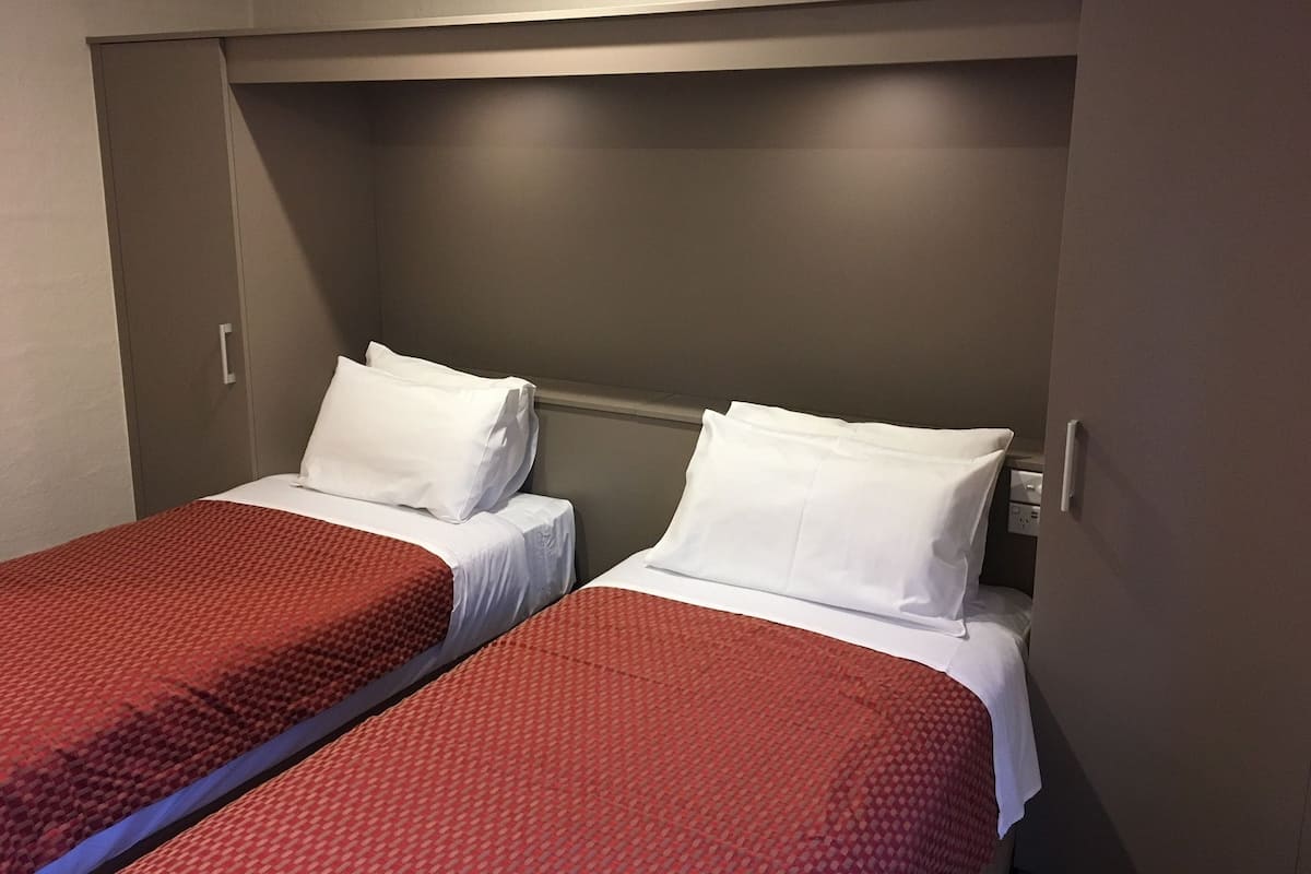 Een hotelkamer met twee bedden, elk voorzien van een rood beddegoed met patroon en witte kussens.