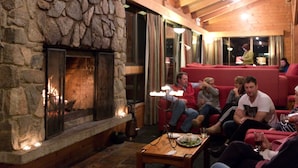 A cozy indoor setting with a stone fireplace, wooden ceiling beams, and red upholstered seating.