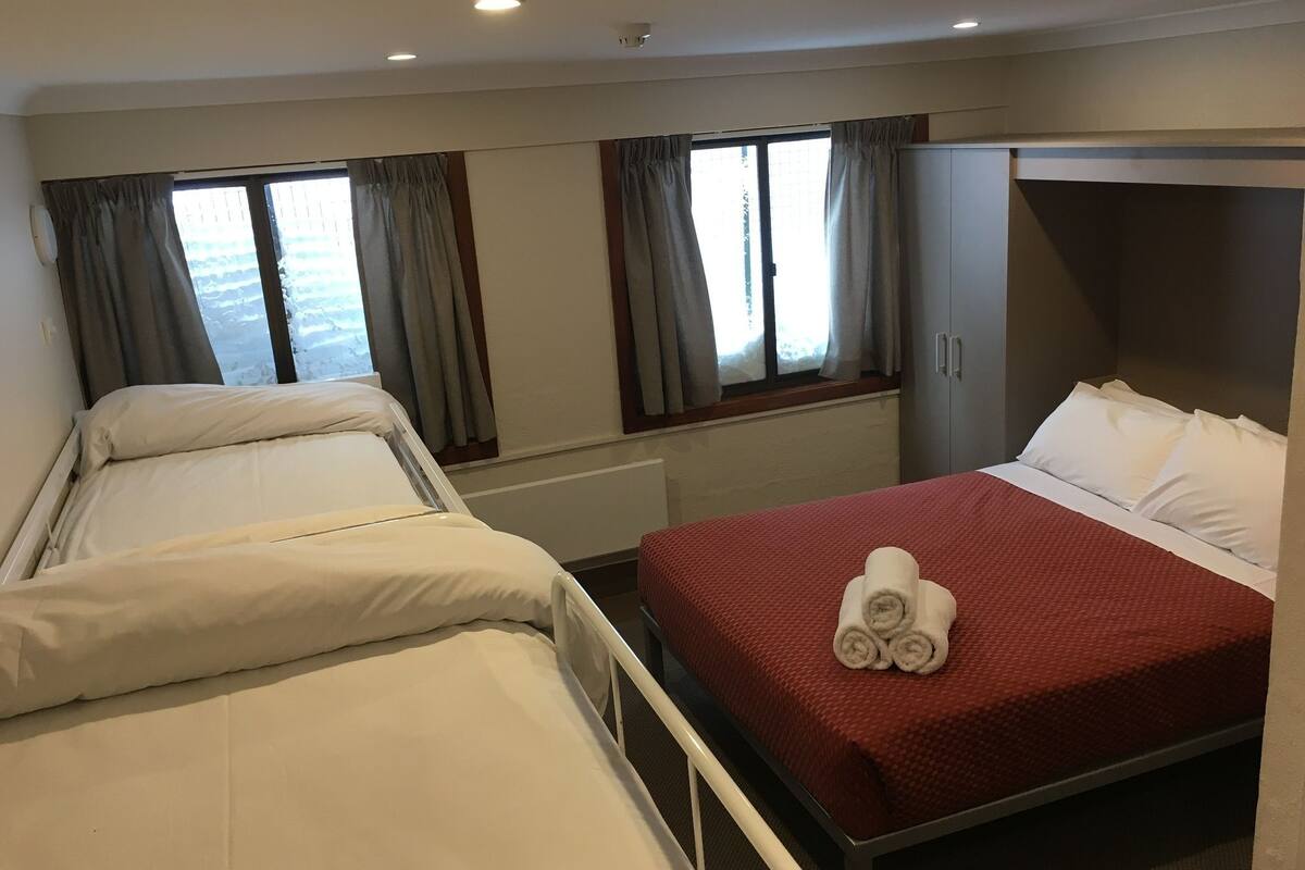 Een hotelkamer met twee bedden, een rode spreideken, witte kussens en een raam met gordijnen.