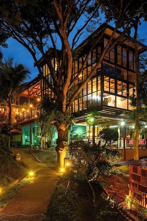 A modern building with a glass facade and wooden structure, surrounded by trees and a pathway. - Vimonsiri Hill Resort & Spa (Chalong)