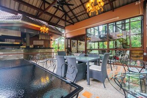 An indoor dining area with glass tables and chairs, a ceiling fan, and a view of the outdoors. - Vimonsiri Hill Resort & Spa (Chalong)