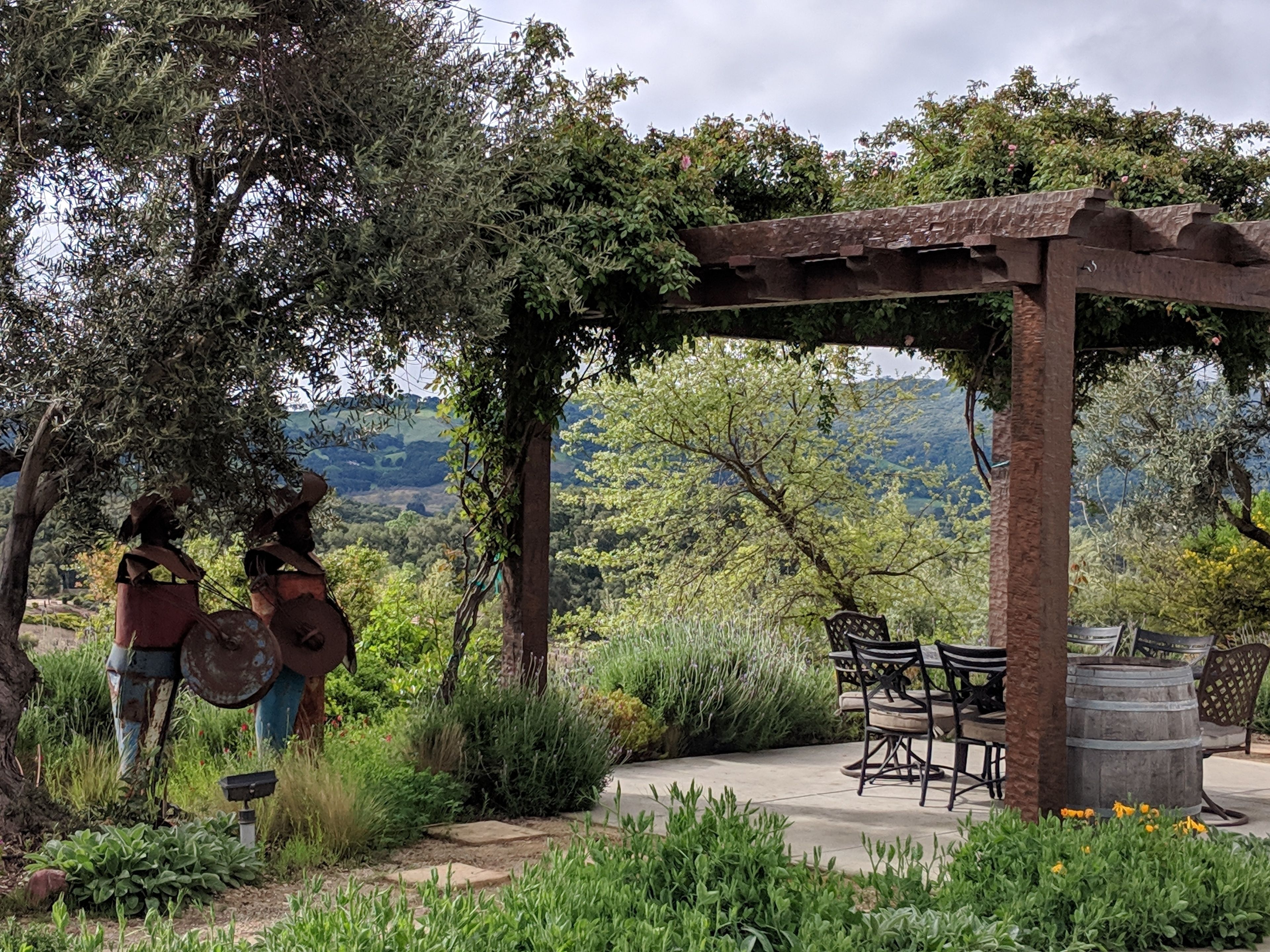 A rustic outdoor seating area with a pergola, stone pathway, and lush greenery.