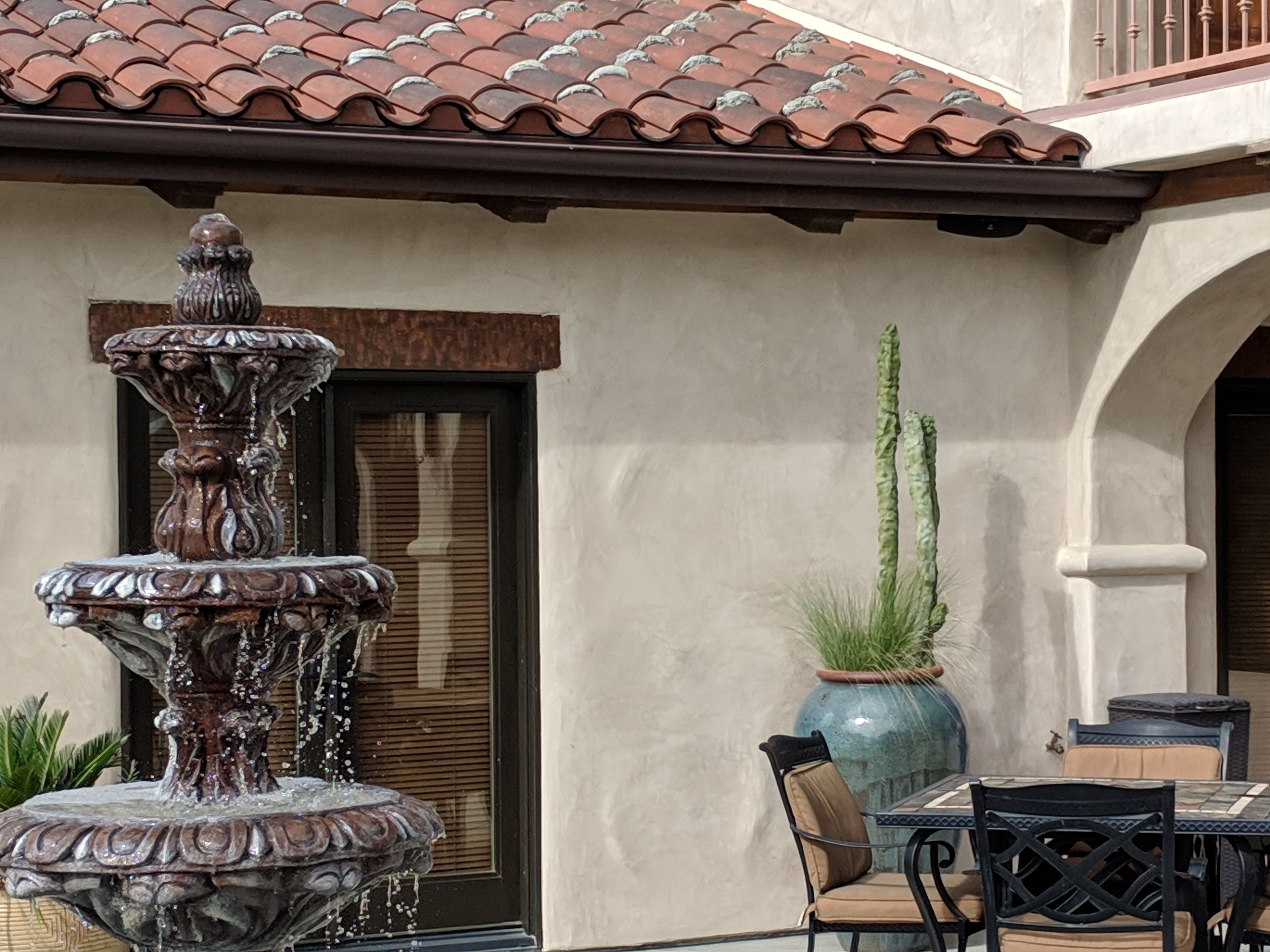 A fountain, a potted plant, and a table with chairs outside a building.