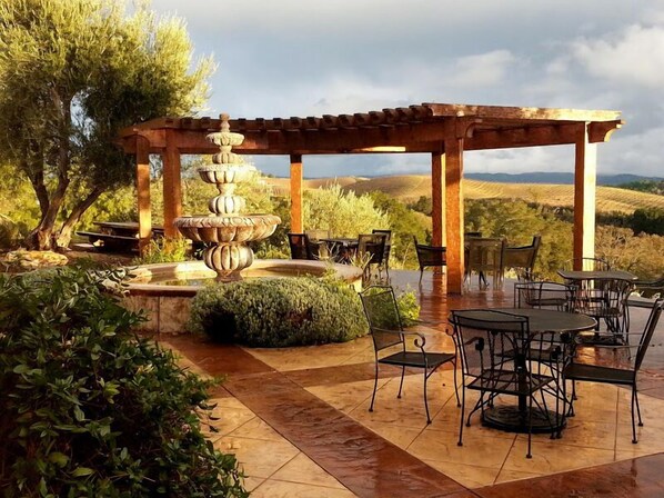 An outdoor patio with a stone fountain, wooden pergola, and seating area overlooking a vineyard. - The Inn at Croad Vineyards (Paso Robles)