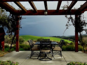 A covered patio with a table and chairs, overlooking a green landscape. - The Inn at Croad Vineyards (Paso Robles)