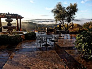An outdoor patio with a fountain, tables, and chairs, surrounded by greenery and overlooking a misty landscape. - The Inn at Croad Vineyards (Paso Robles)