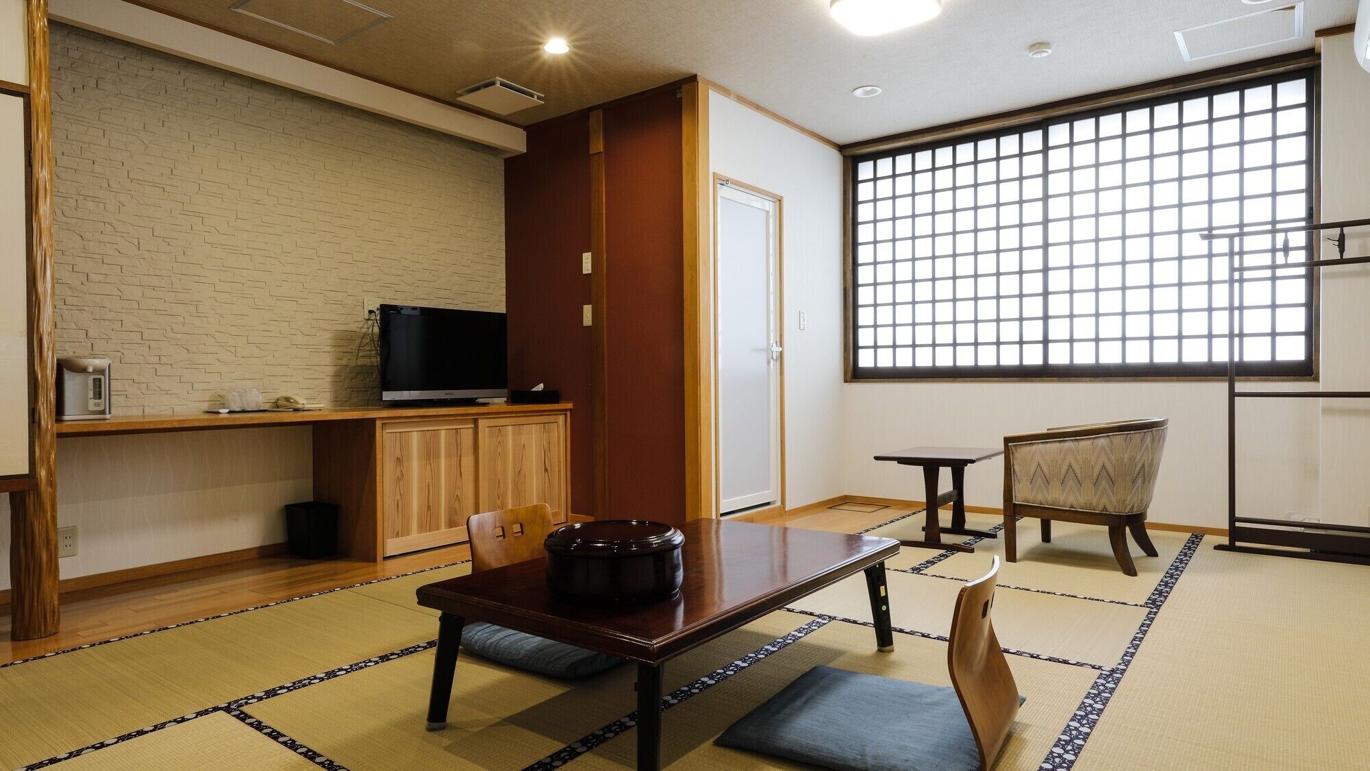 Une pièce de style japonais traditionnel, avec un sol recouvert de tatamis, un téléviseur posé sur une étagère en bois, une table laquée noire et une porte coulissante.
