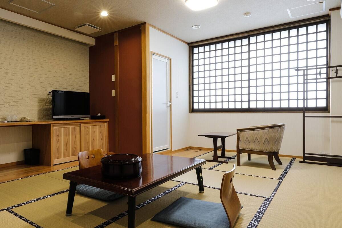 A traditional Japanese room with tatami flooring, a television on a wooden shelf, a black lacquered table, and a sliding door.