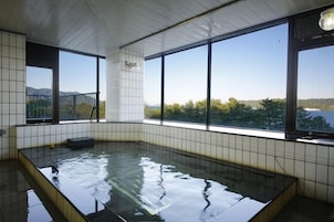 Un jacuzzi con paredes de azulejos y ventanas amplias que ofrecen vistas a un paisaje montañoso.