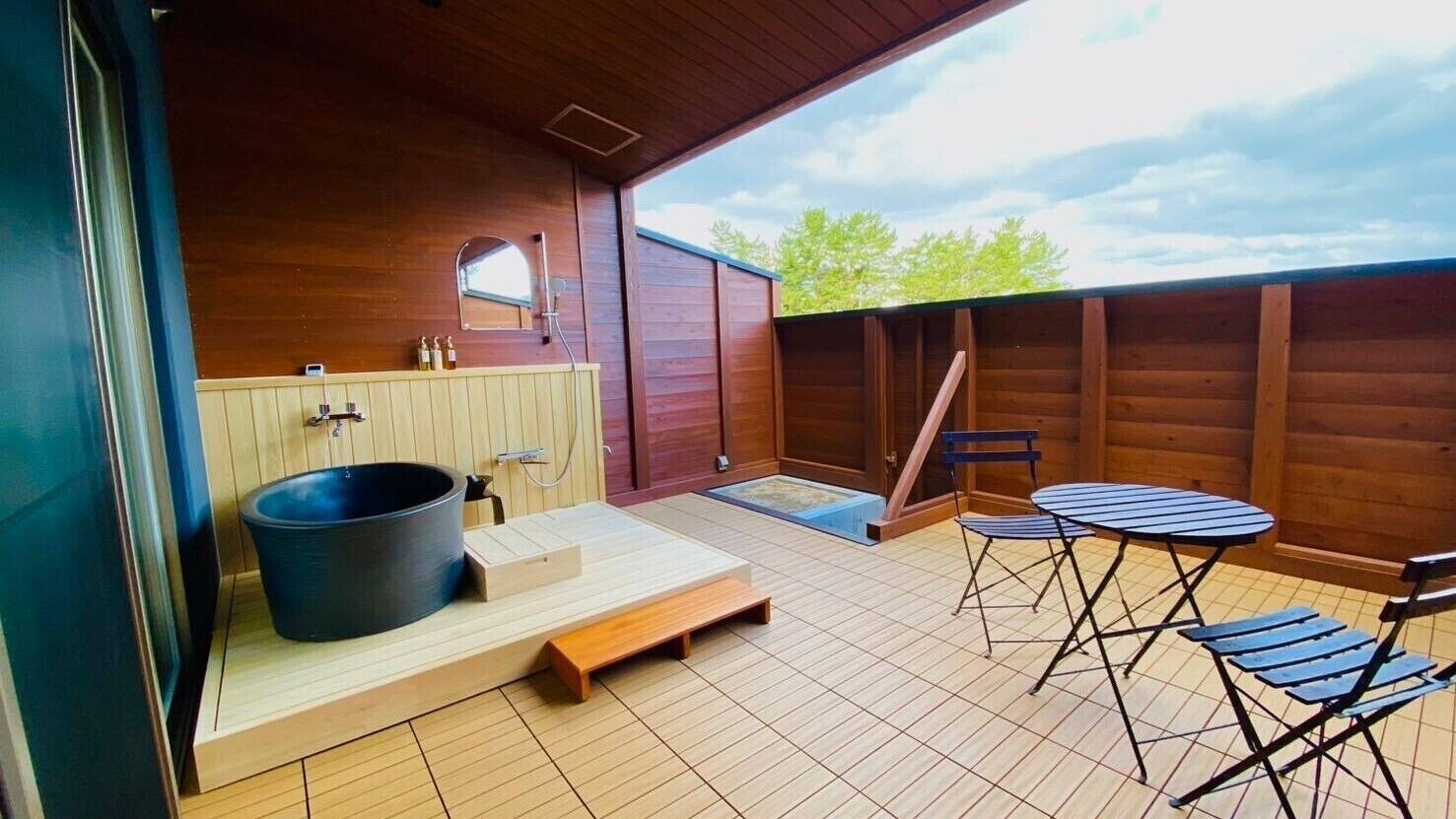 Una terraza de madera con un jacuzzi, una pequeña mesa y sillas.