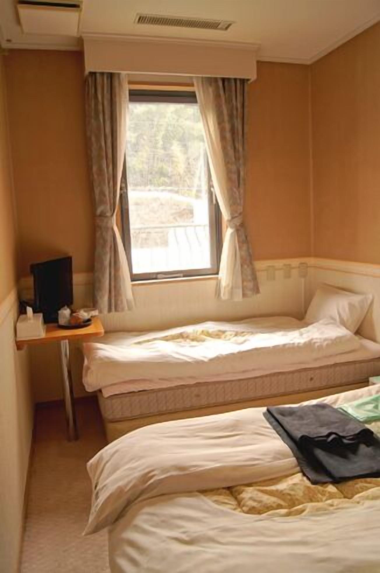 Una habitación de hotel pequeña con una cama individual, un escritorio con silla y una ventana con cortinas.