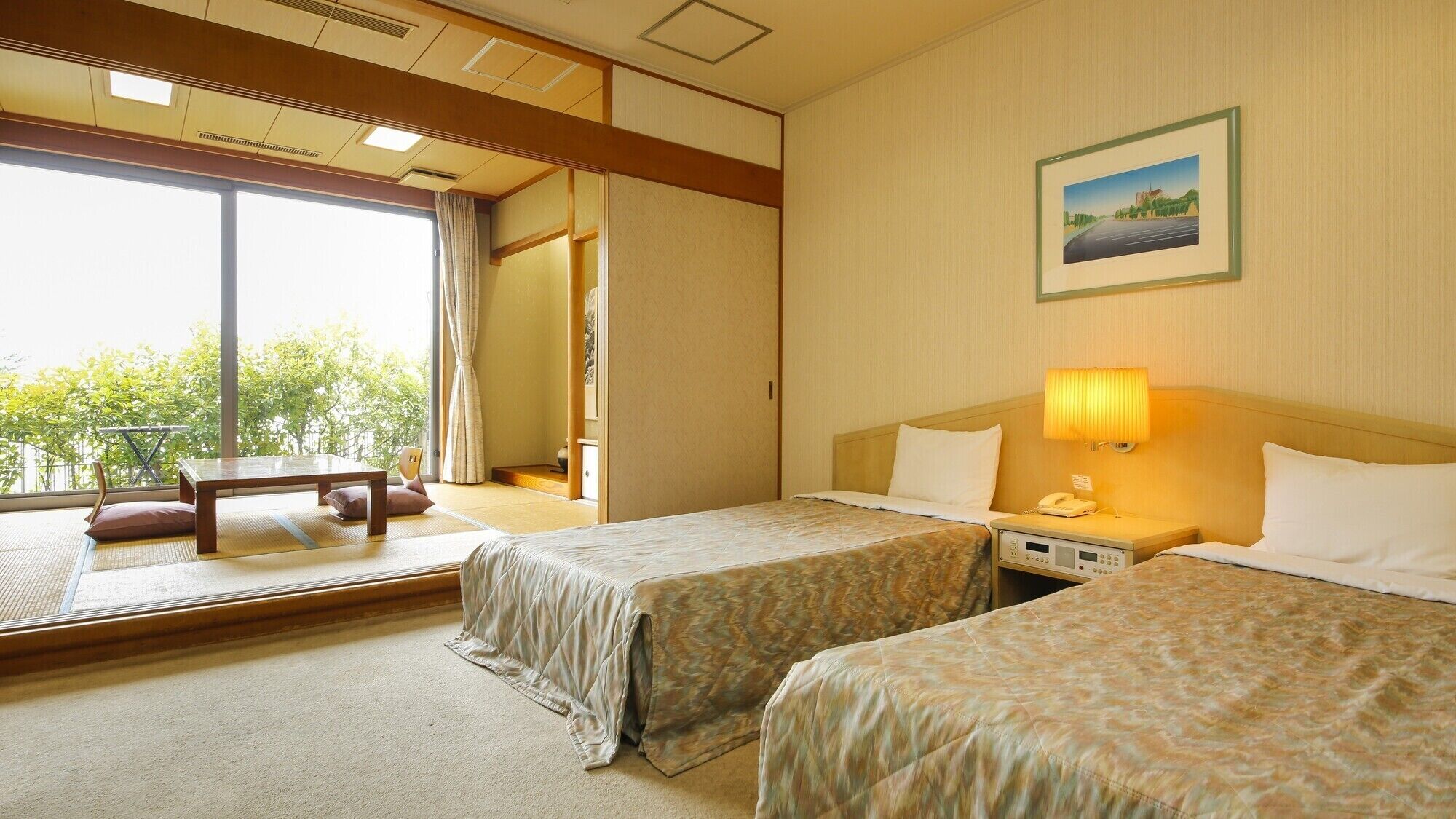 Une chambre d’hôtel avec deux lits, un bureau, une chaise, une fenêtre donnant sur un paysage agréable, un tableau au mur et une lampe de chevet.