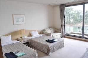 A hotel room with two beds, a desk with a lamp, a chair, and a large window with a view of trees and water. - Amano Hashidate So (Miyazu)
