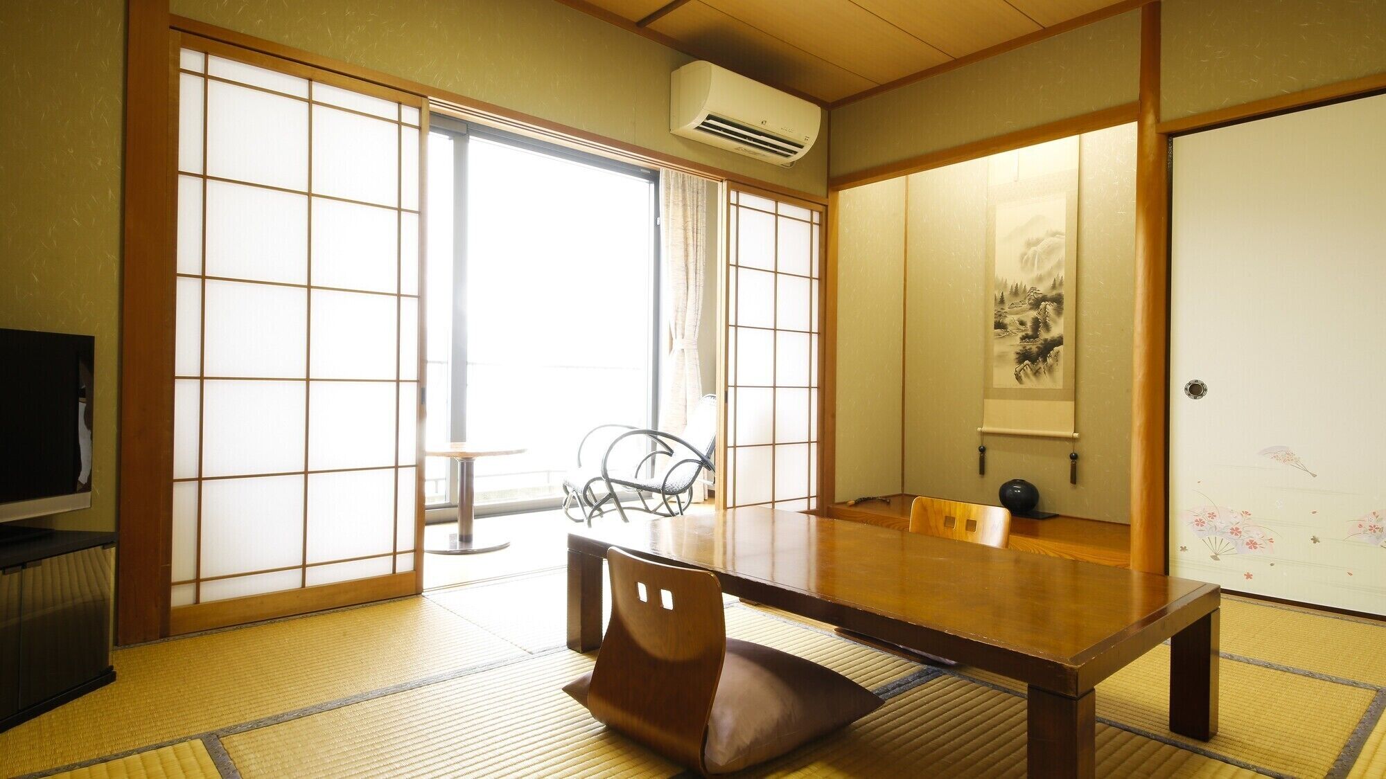 Une pièce de style japonais traditionnel, avec un sol recouvert de tatamis, une petite table basse, une chaise, des portes coulissantes et un climatiseur fixé au mur.