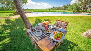 An outdoor dining area with a table set for breakfast, including fruits, pastries, and beverages, overlooking a swimming pool and lush greenery. - Kithala Resort (Thissamaharama)