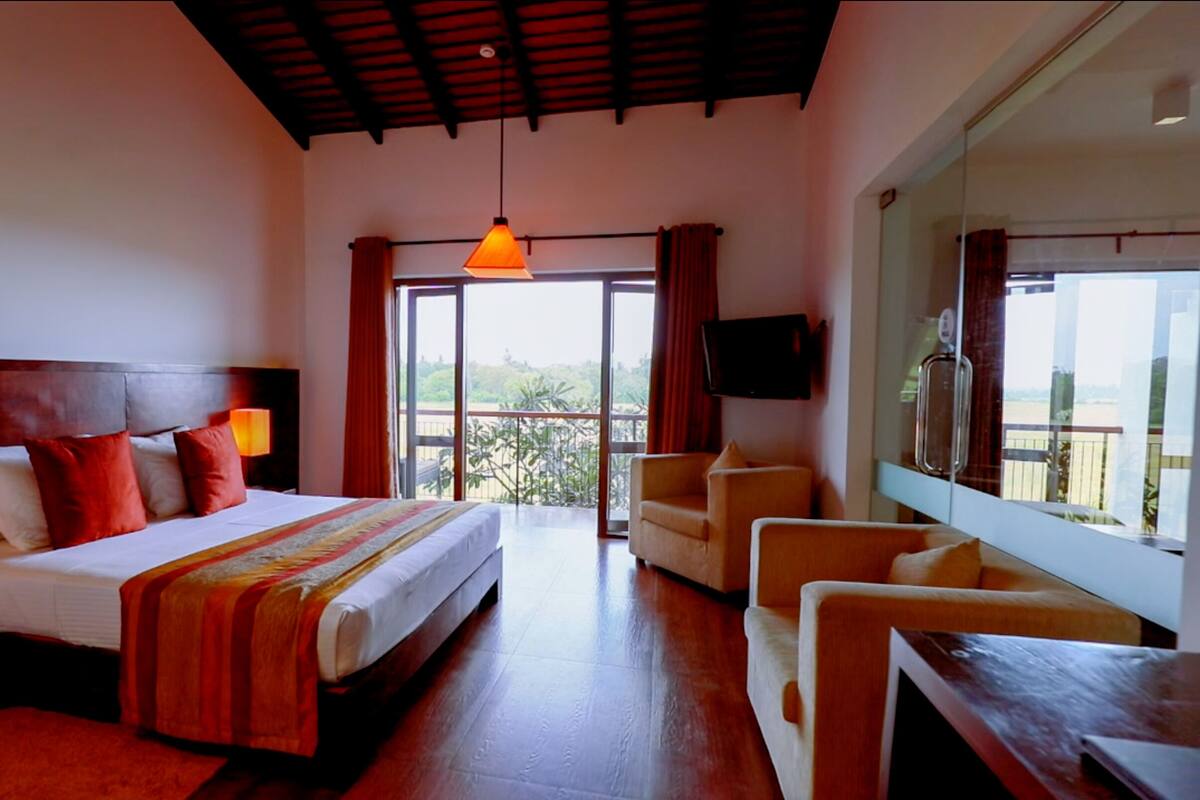 A hotel room with a large bed, a TV, a balcony with a view, and a wooden ceiling.