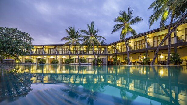 A hotel with a pool reflecting palm trees and a building with balconies. - Kithala Resort (Thissamaharama)