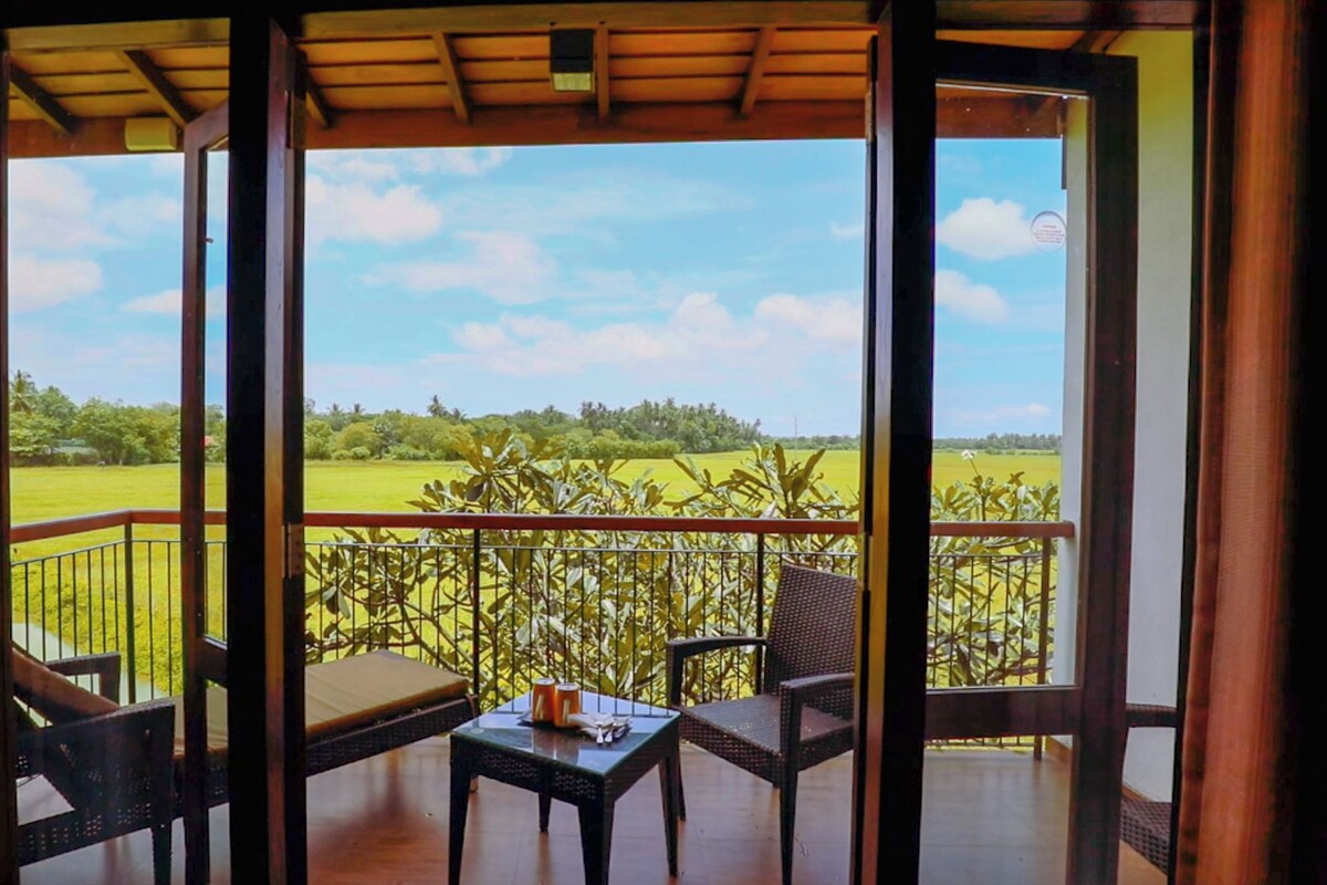 A balcony with a table and chairs, overlooking a green field.