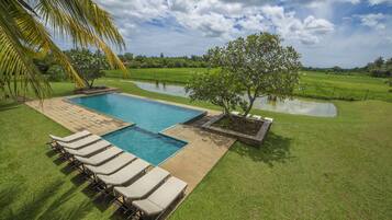 A swimming pool with lounge chairs, surrounded by a grassy area and a small pond.