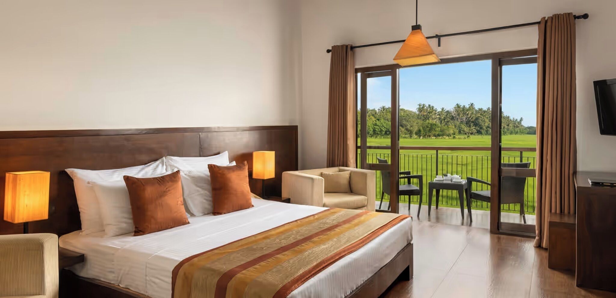 Quarto de hotel com uma cama grande, um sofá, uma varanda com vista para um campo de golfe e uma televisão na parede.