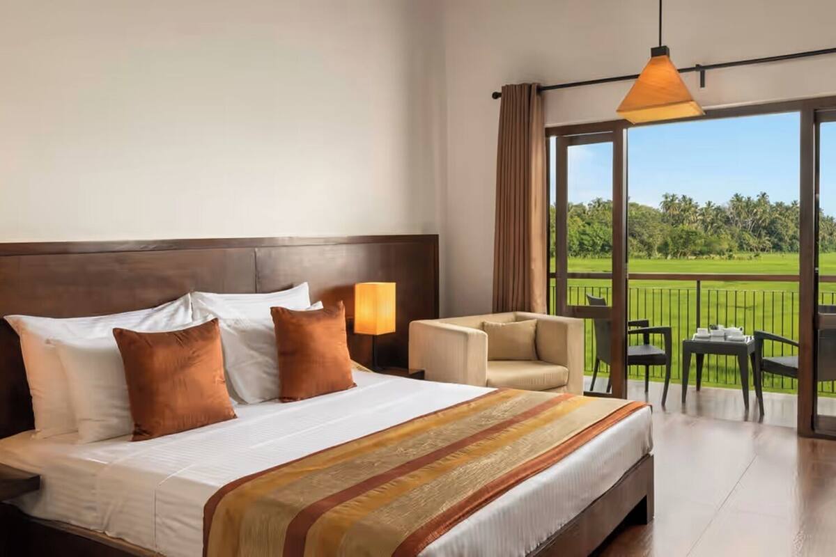 A hotel room with a large bed, a sofa, a balcony with a view of a golf course, and a TV on the wall.