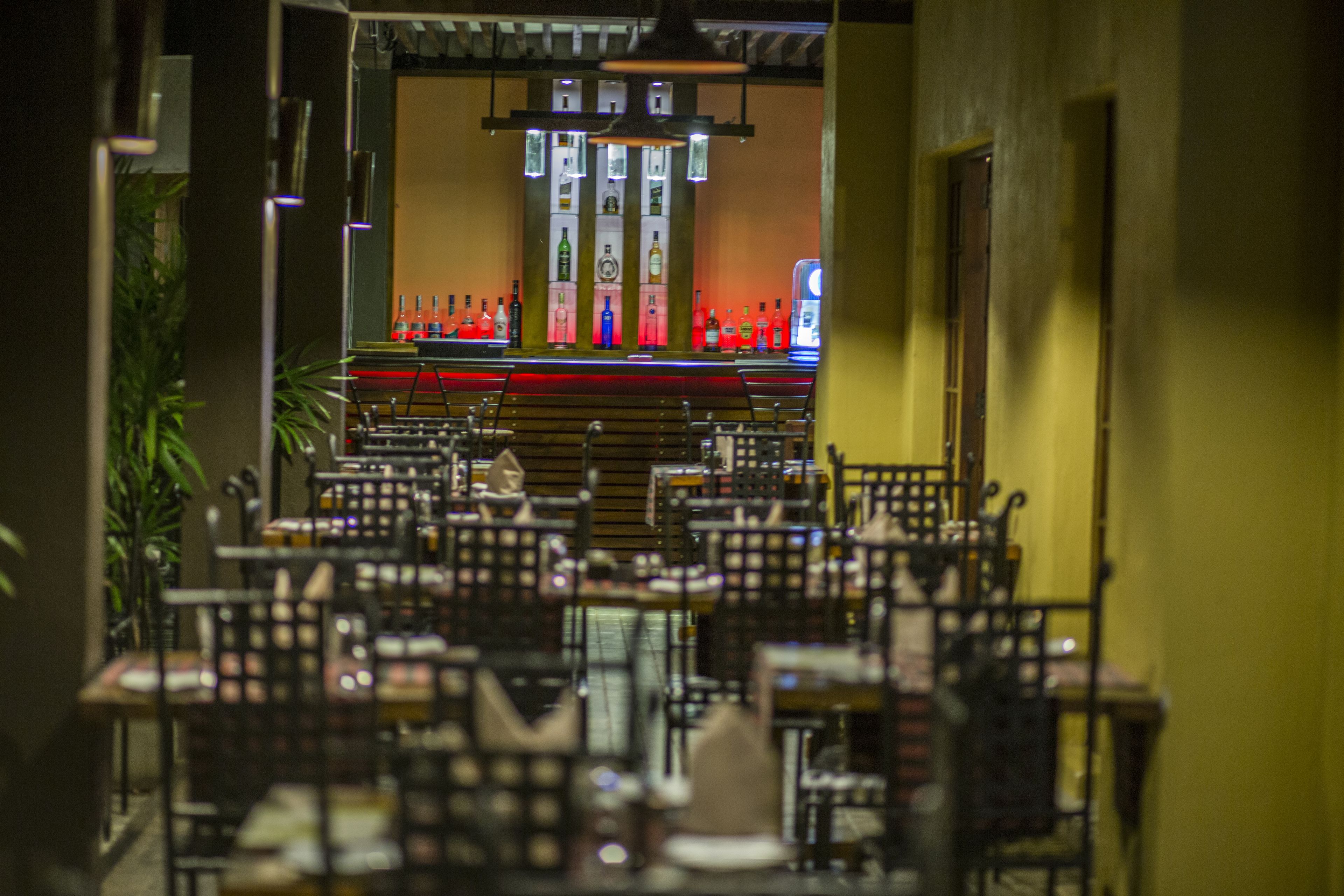 A restaurant with a long counter, multiple chairs, and a bar area with bottles.