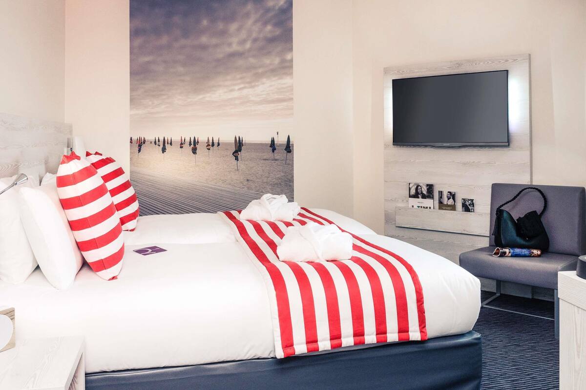 A hotel room with a bed, a flat-screen TV mounted on the wall, and a beach scene mural.