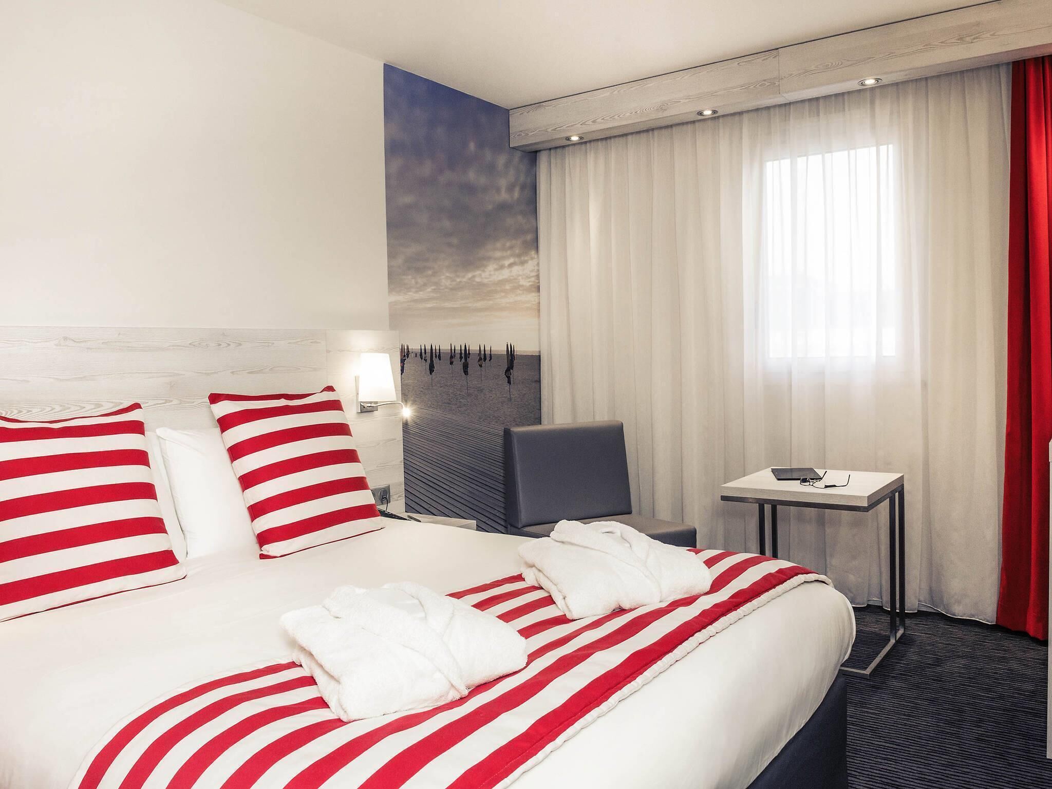 A hotel room with a bed, a desk, a chair, and a view of the sky through the window.