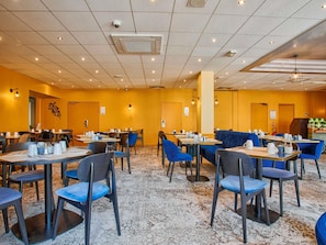 Een restaurantruimte in een hotel met tafels, stoelen, plafondlampen en een beveiligingscamera.