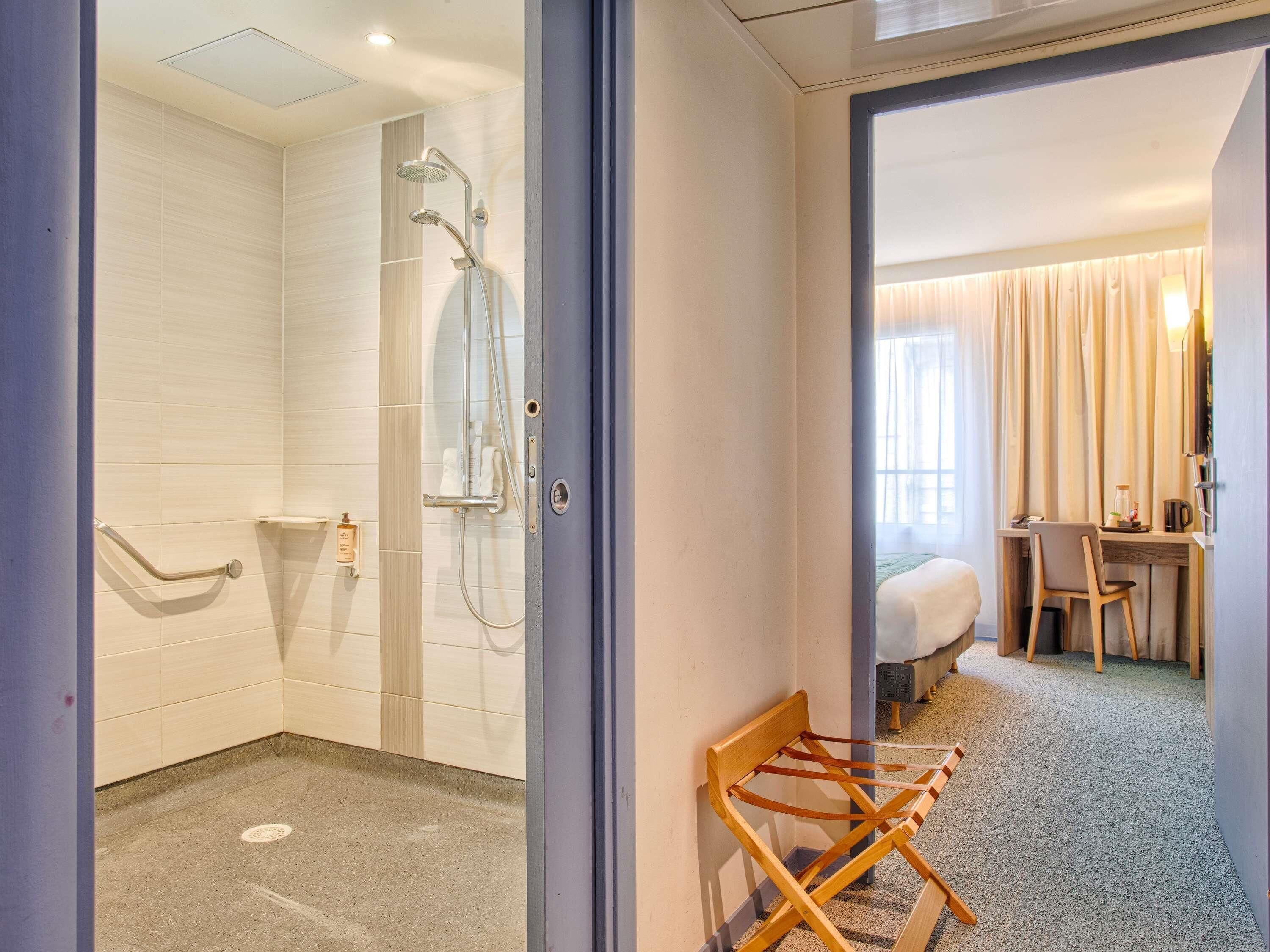 A hotel room with a shower, a bed, a desk, and a chair.