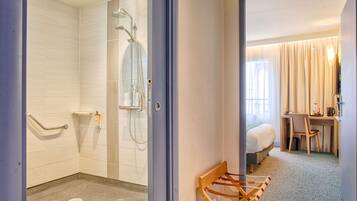A hotel room with a shower, a bed, a desk, and a chair.