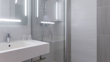 A modern bathroom with a glass-enclosed shower, a white sink, and a mirror with integrated lighting.