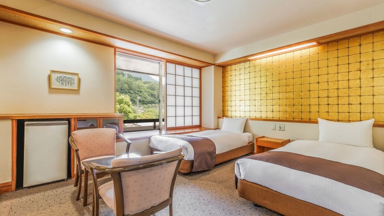 A hotel room with two beds, a desk, a chair, and a view of greenery outside.