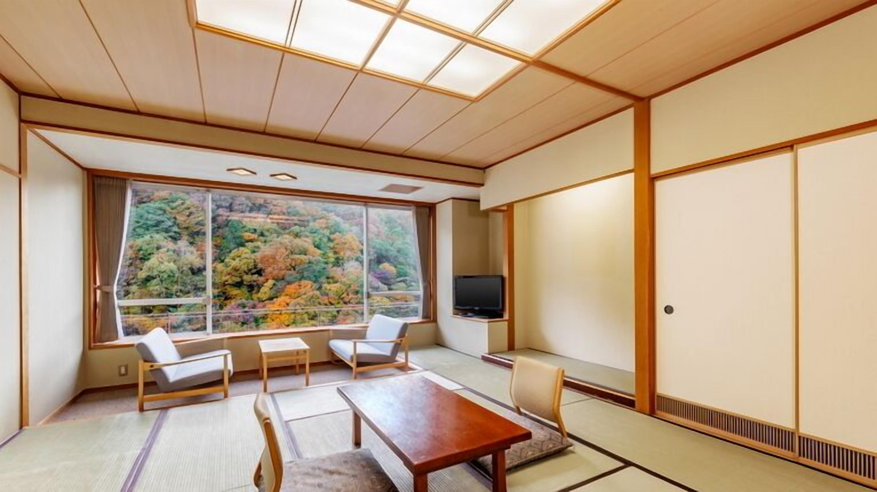 A traditional Japanese room with tatami flooring, a low table, two chairs, a television, and a sliding door.
