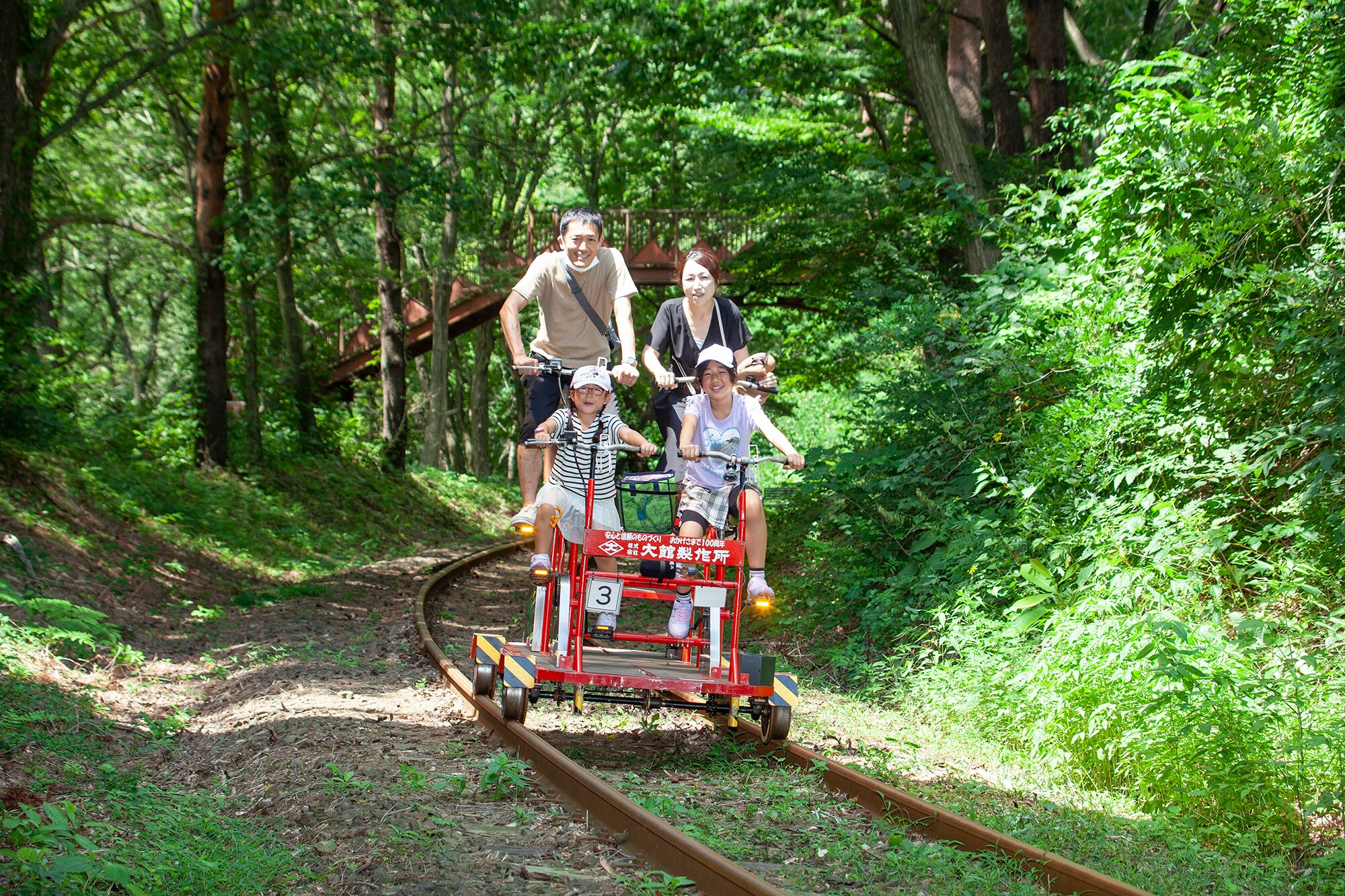 A group of people riding a small train on a railway track surrounded by dense greenery.