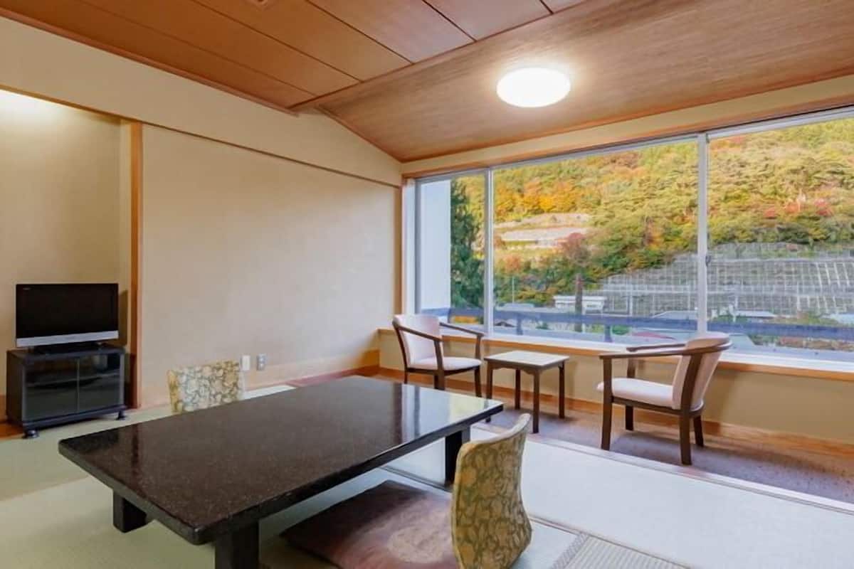 A room with a TV, a table, and chairs, a window with a view of trees.