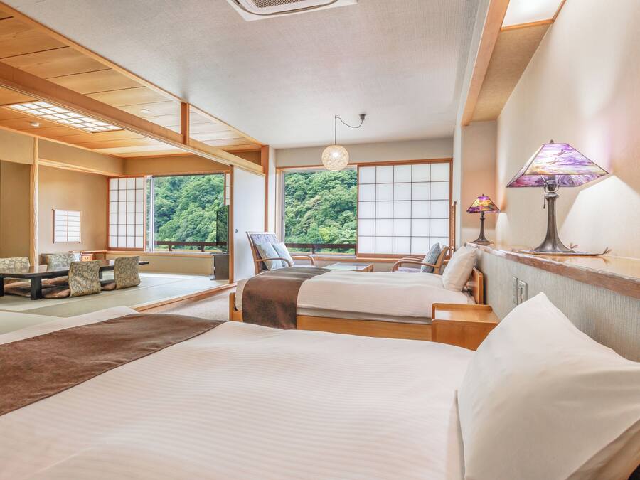 Una habitación tradicional japonesa con suelo de tatami, dos camas con ropa de cama blanca, techo de madera y vistas a un follaje exuberante.