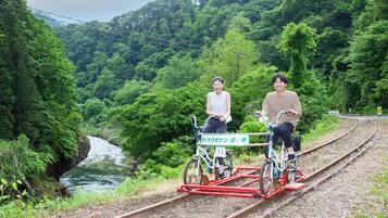 Dos personas montando en bicicleta sobre vías de tren, rodeadas de abundante vegetación y un río.