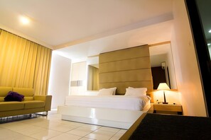 A hotel room with a bed, a sofa, a nightstand, and a lamp.
